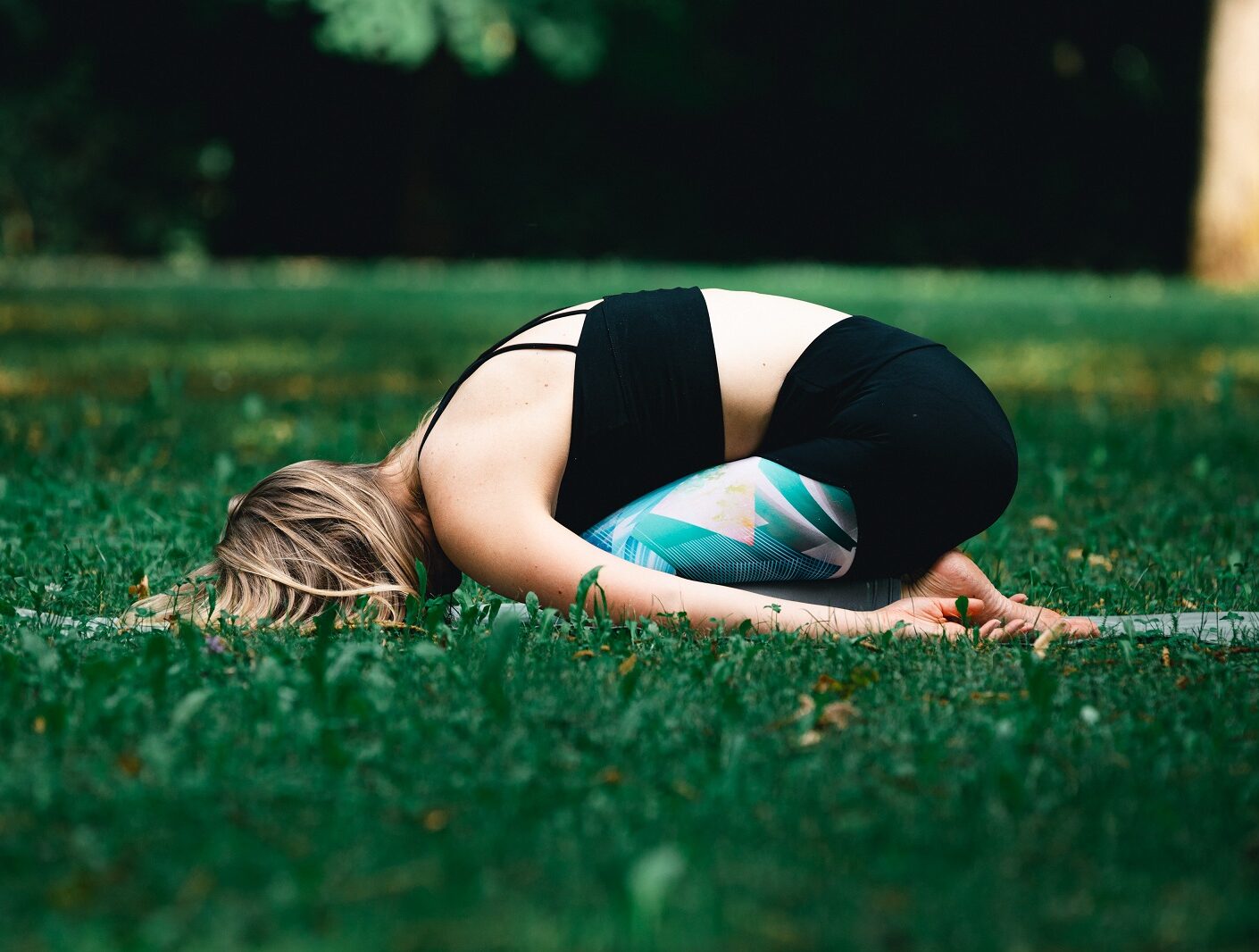 Eine Frau übt Yoga in der Wiese und nimmt die Stellung des Kindes ein.
