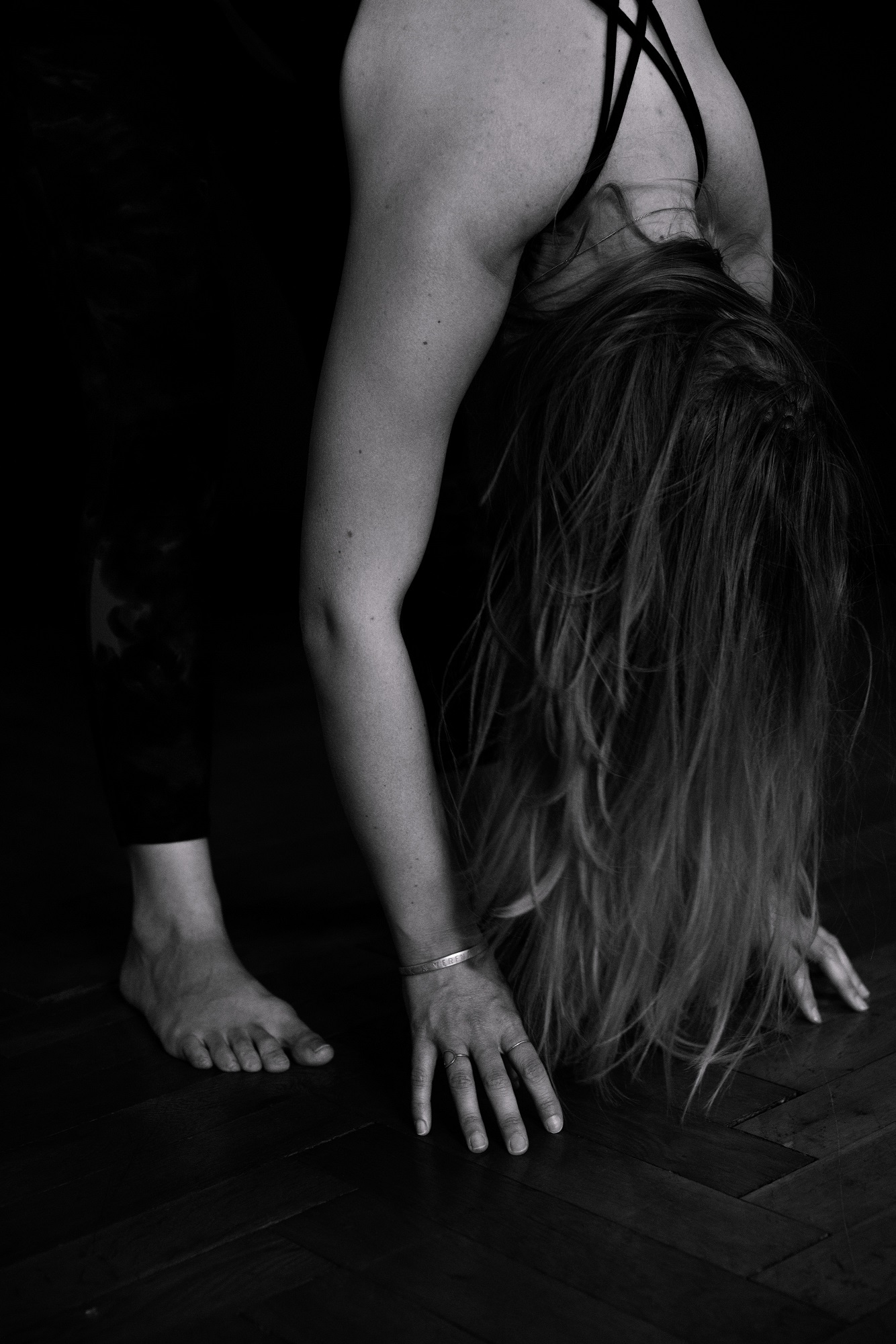 Eine Frau übt die stehende Vorwärtsbeuge, im Yoga nennt sich diese Uttanasana. Die Finger berühren leicht den Boden. Die Frau ist völlig entspannt.